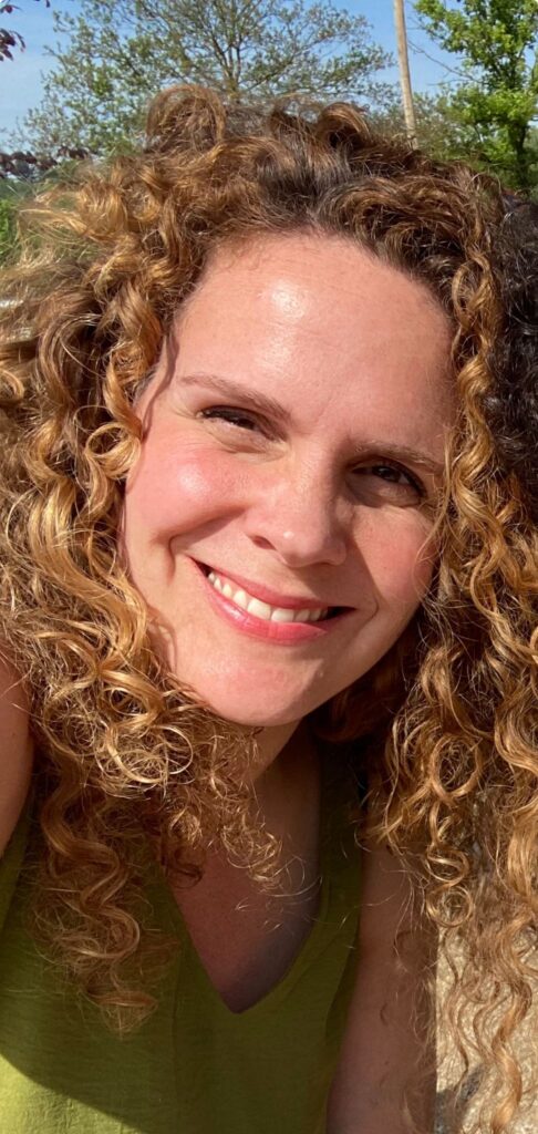 foto van Anne, een vrolijk lachende vrouw met lang rossig donkerblond haar in de zon.